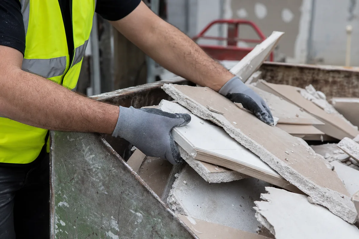 Artisan chargeant des plaques de plâtre déposées dans une benne de tri sur un chantier de rénovation