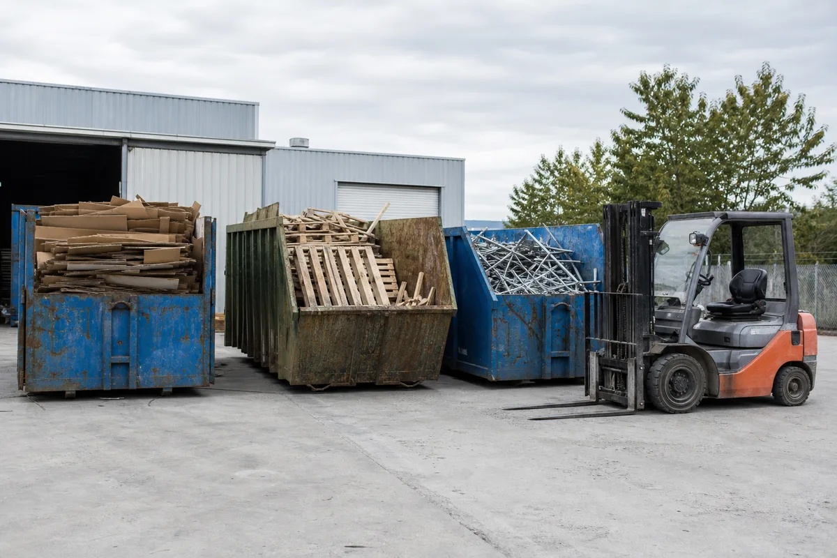 Bennes de tri sélectif alignées dans la cour logistique d’une entreprise